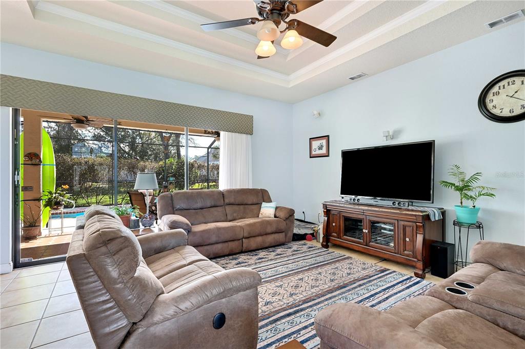 A living room features brown reclining sofas, a television on a wooden stand, and sliding doors — 13855 RUDI LOOP, SPRING HILL, FL