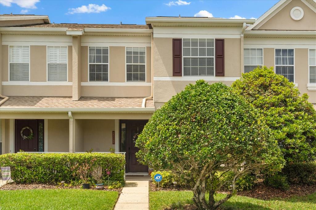 A two-story townhouse exterior features tan stucco walls, dark shutters, and a front walkway — 1530 TALLY CIRCLE, OVIEDO, FL