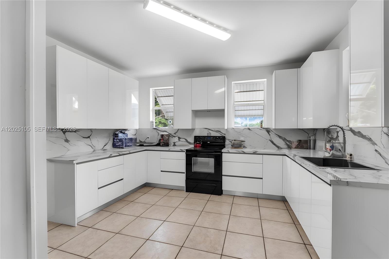 A kitchen features white flat-panel cabinets, marble-patterned countertops, a black stove, and tiled flooring — 137 NW 20th St, Homestead FL 33030, HOMESTEAD, FL