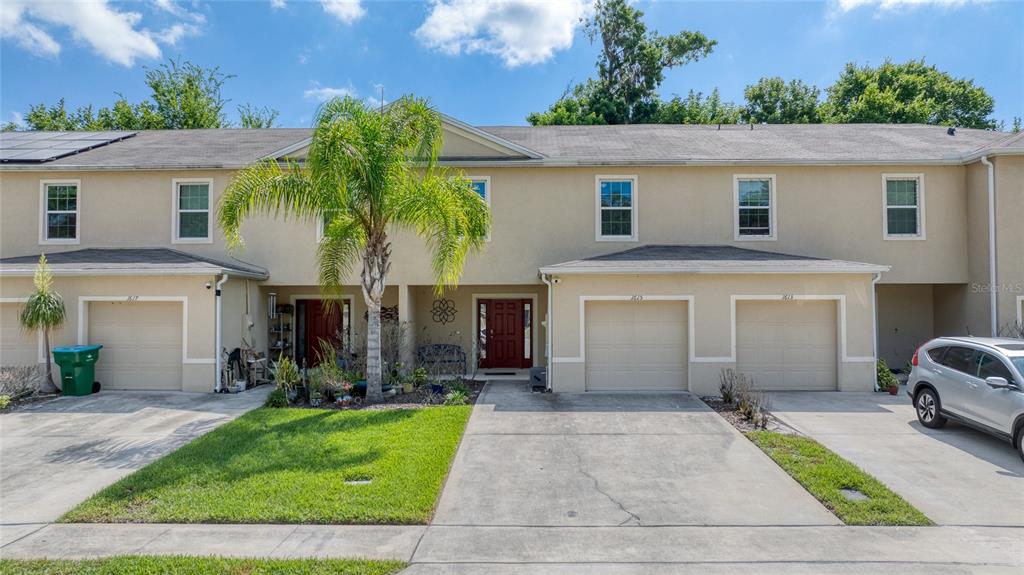 A row of beige townhouses features garages, concrete driveways, and a central palm tree — 1615 PRIMO COURT, DAYTONA BEACH, FL