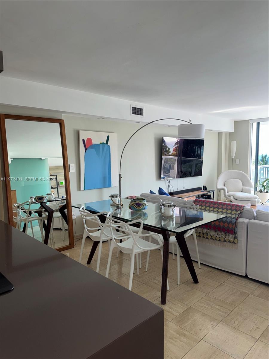 A dining area with a glass table and white chairs sits beside a large mirror — 2457 Collins Ave # 405, Miami Beach FL 33140, MIAMI BEACH, FL