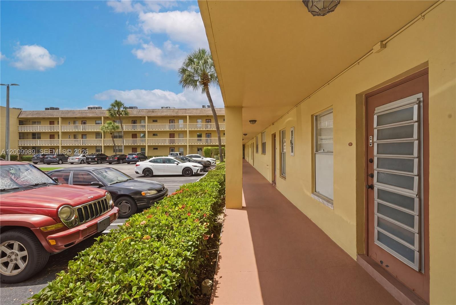 An exterior walkway leads past apartment doors along a yellow building with a parking lot — 5961 NW 61st Ave # 111, Tamarac FL 33319, TAMARAC, FL