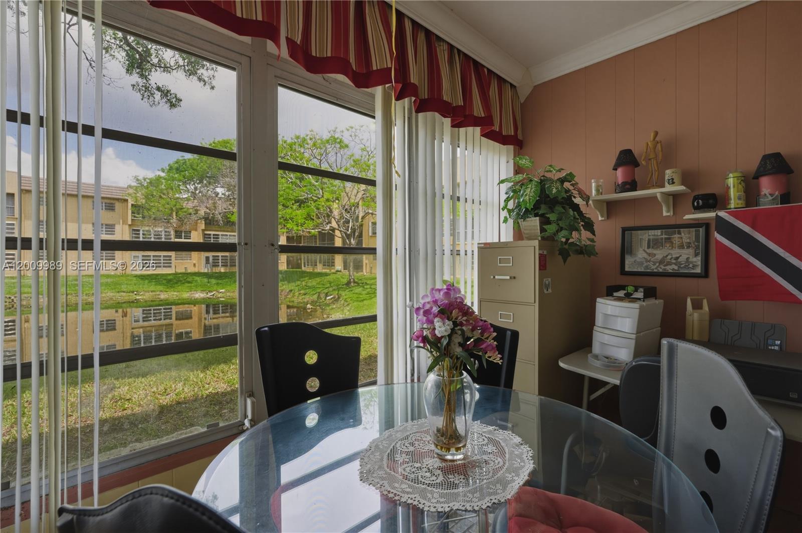 A sunroom features a glass dining table, vertical blinds, and a view of a pond — 5961 NW 61st Ave # 111, Tamarac FL 33319, TAMARAC, FL