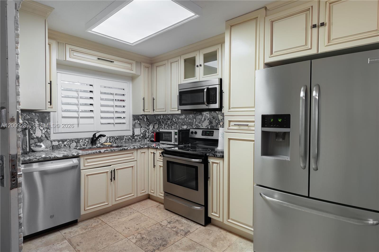 A kitchen features cream-colored cabinets, stainless steel appliances, and a dark patterned stone backsplash — 420 Celestial Way # 101, Juno Beach FL 33408, JUNO BEACH, FL
