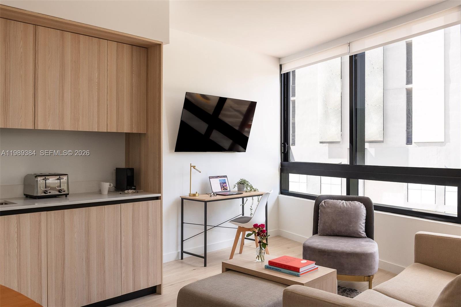 A bedroom features a bed with white linens, a large window, and a circular wall mirror — 225 N Miami Ave # 202, Miami FL 33128, MIAMI, FL