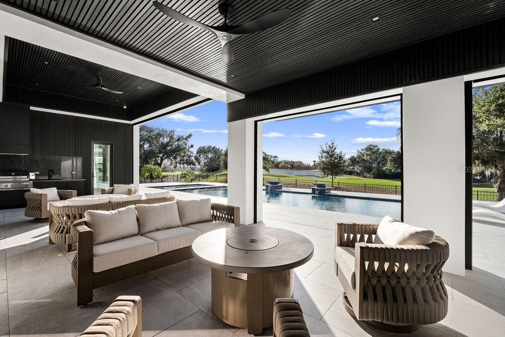 A covered outdoor patio features a fire pit, lounge seating, and a pool overlooking a golf course — 5074 ISLEWORTH COUNTRY CLUB DRIVE, WINDERMERE, FL
