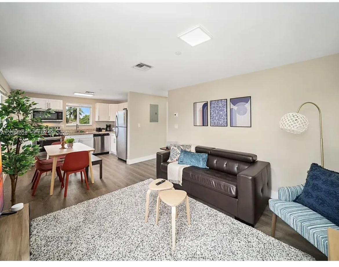 An open-concept living and dining area features a dark leather sofa, wood-look flooring, and kitchen — 2311 Scott St # 2, Hollywood FL 33020, HOLLYWOOD, FL