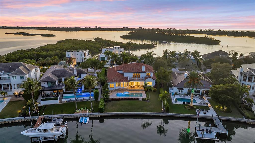 An aerial view shows waterfront homes with swimming pools, private docks, and boats at sunset — 1389 TANGIER WAY, SARASOTA, FL