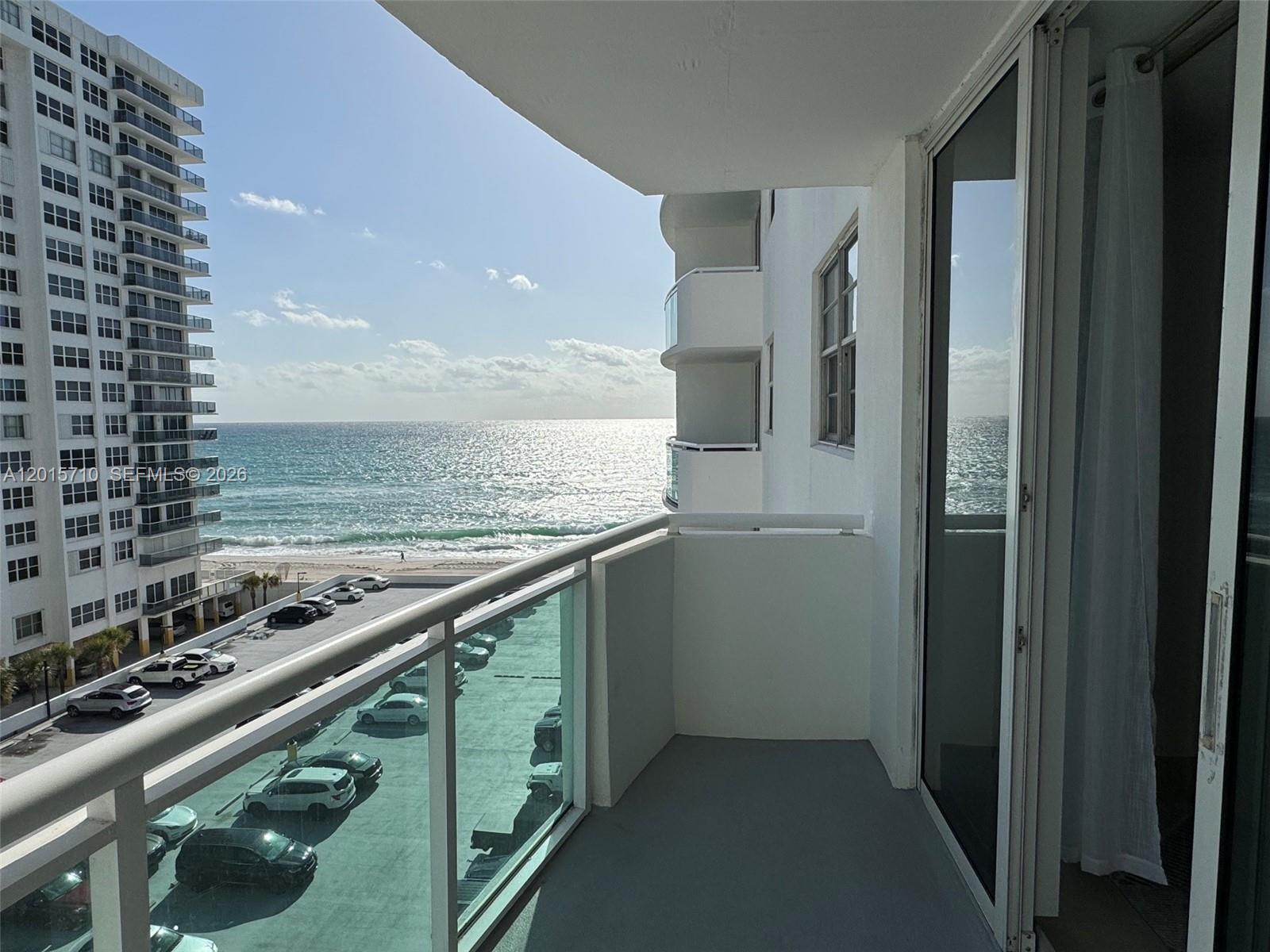 A balcony with a glass railing overlooks a parking lot and the ocean — 3001 S Ocean Dr # 703, Hollywood FL 33019, HOLLYWOOD, FL