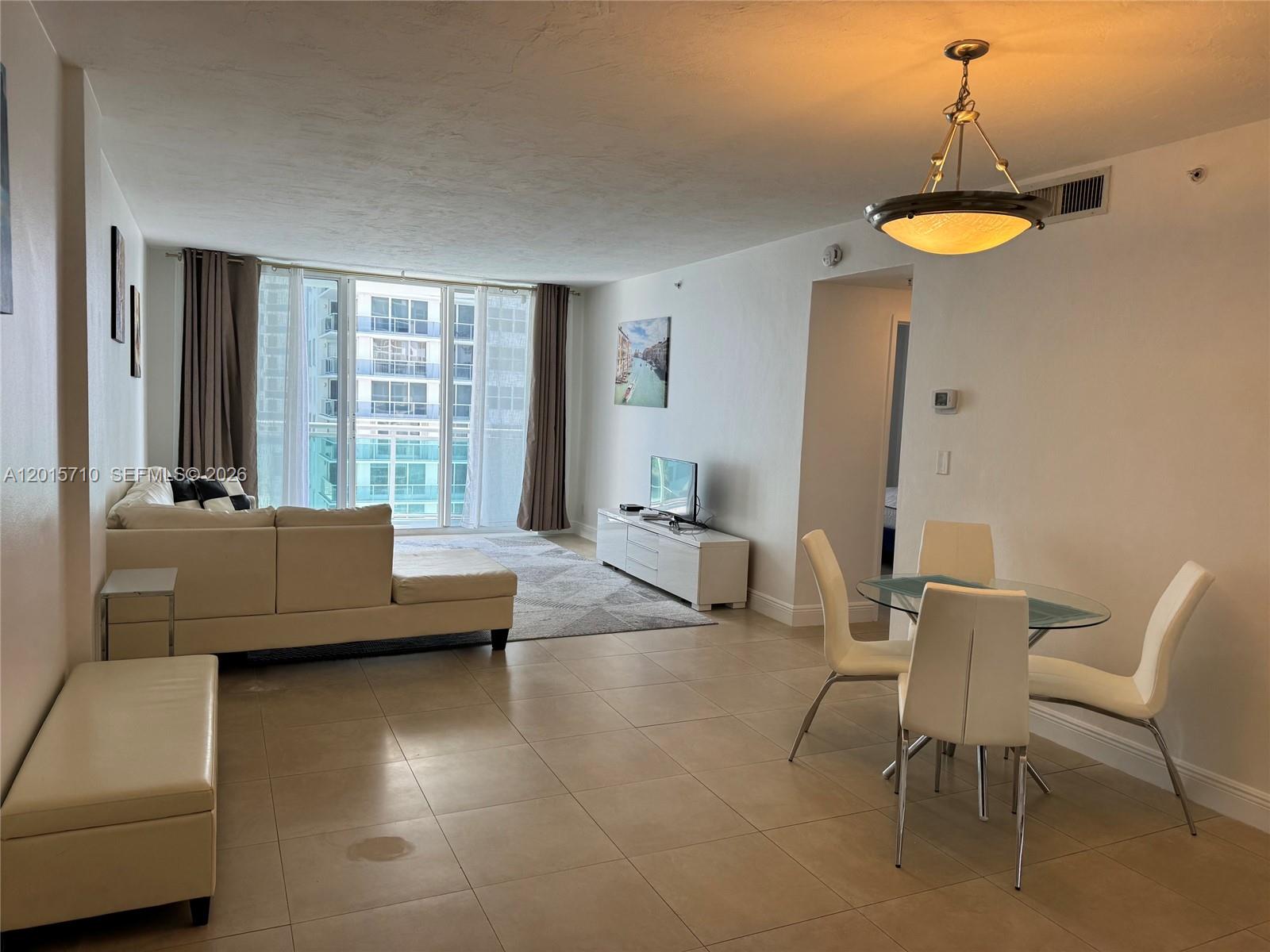 An open-concept living and dining area features tile flooring, a sectional sofa, and floor-to-ceiling windows — 3001 S Ocean Dr # 703, Hollywood FL 33019, HOLLYWOOD, FL