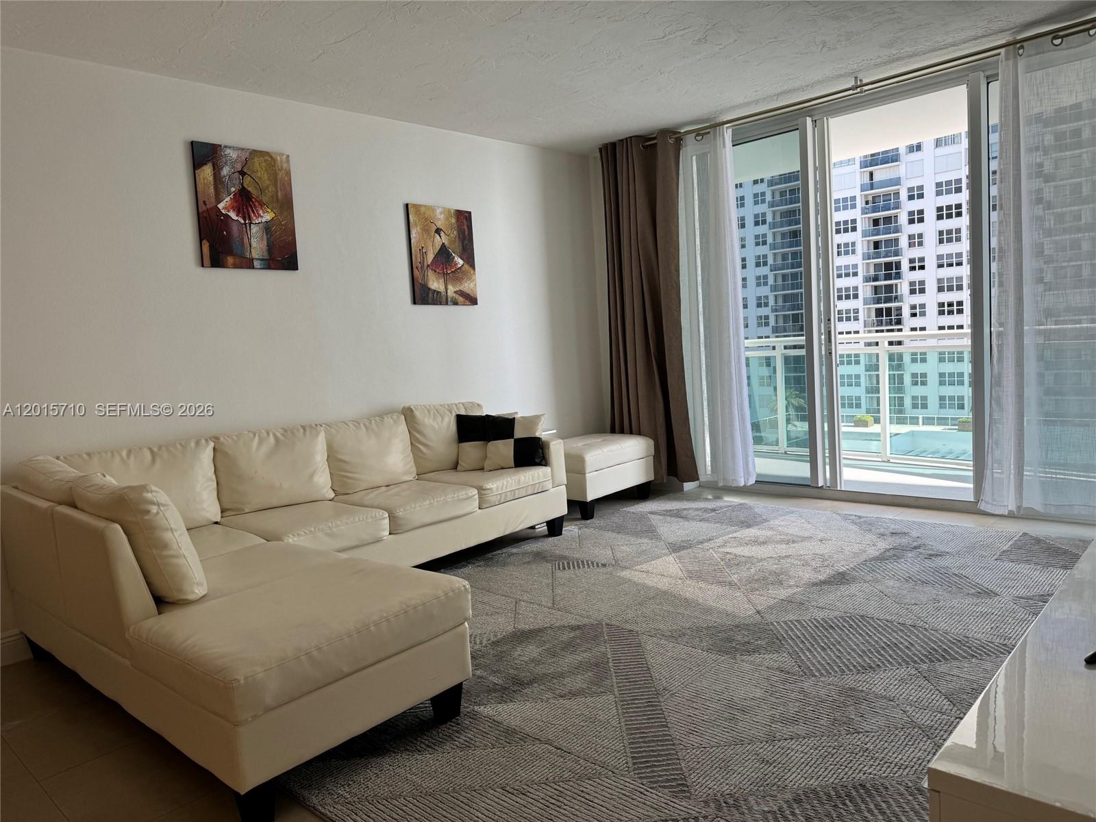 A living room features a white sectional sofa, a geometric rug, and a balcony view — 3001 S Ocean Dr # 703, Hollywood FL 33019, HOLLYWOOD, FL