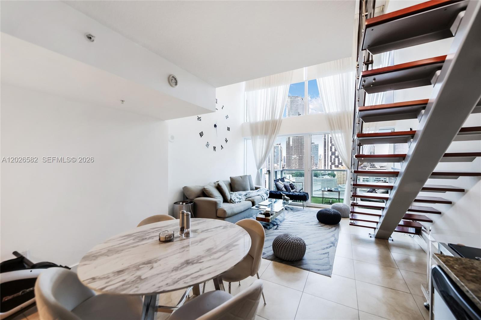 A modern living and dining area features high ceilings, a floating staircase, and floor-to-ceiling windows — 41 SE 5th St # 1303, Miami FL 33131, MIAMI, FL