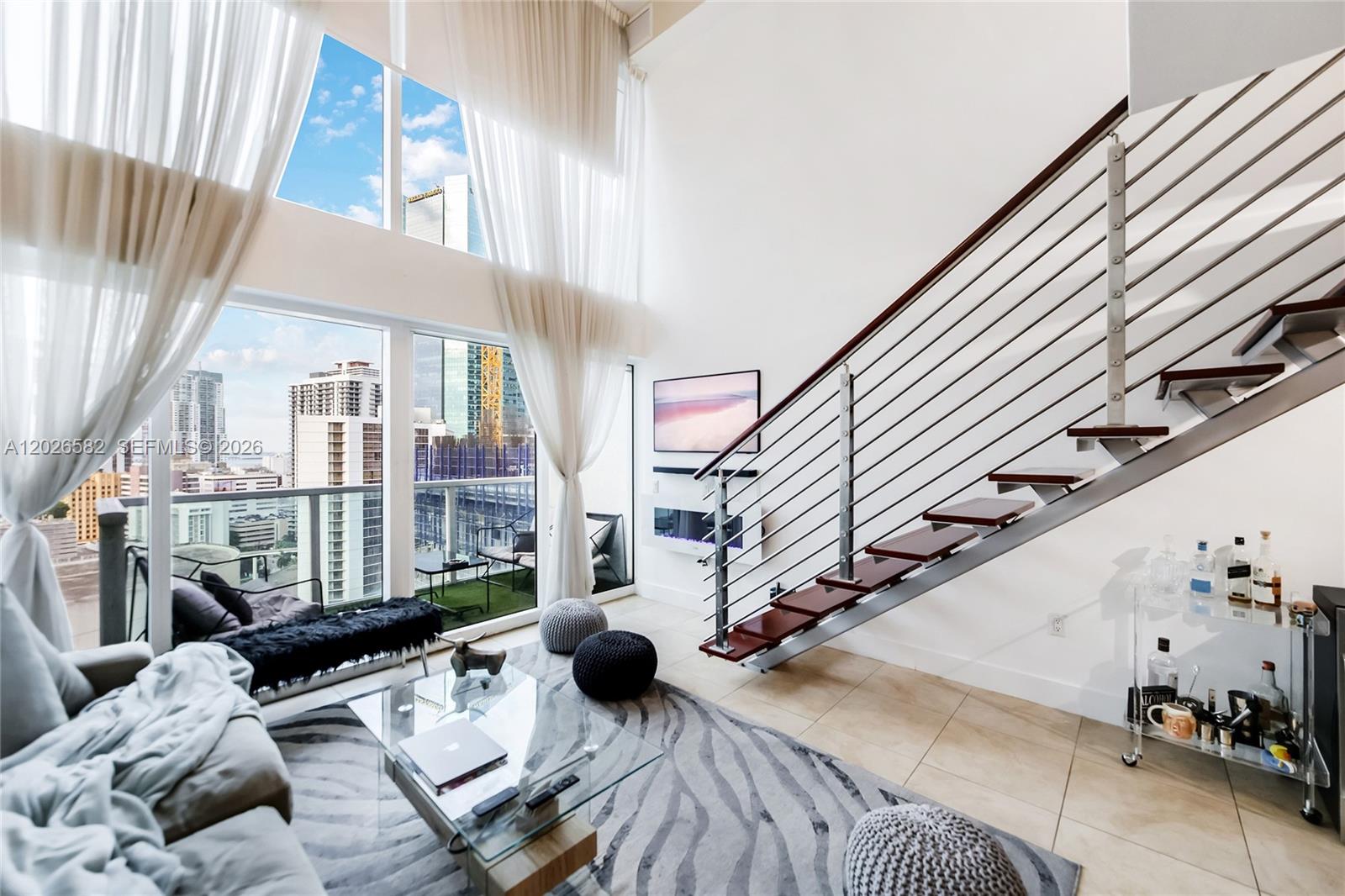 A modern living room features a double-height ceiling, floor-to-ceiling windows, and an open staircase — 41 SE 5th St # 1303, Miami FL 33131, MIAMI, FL