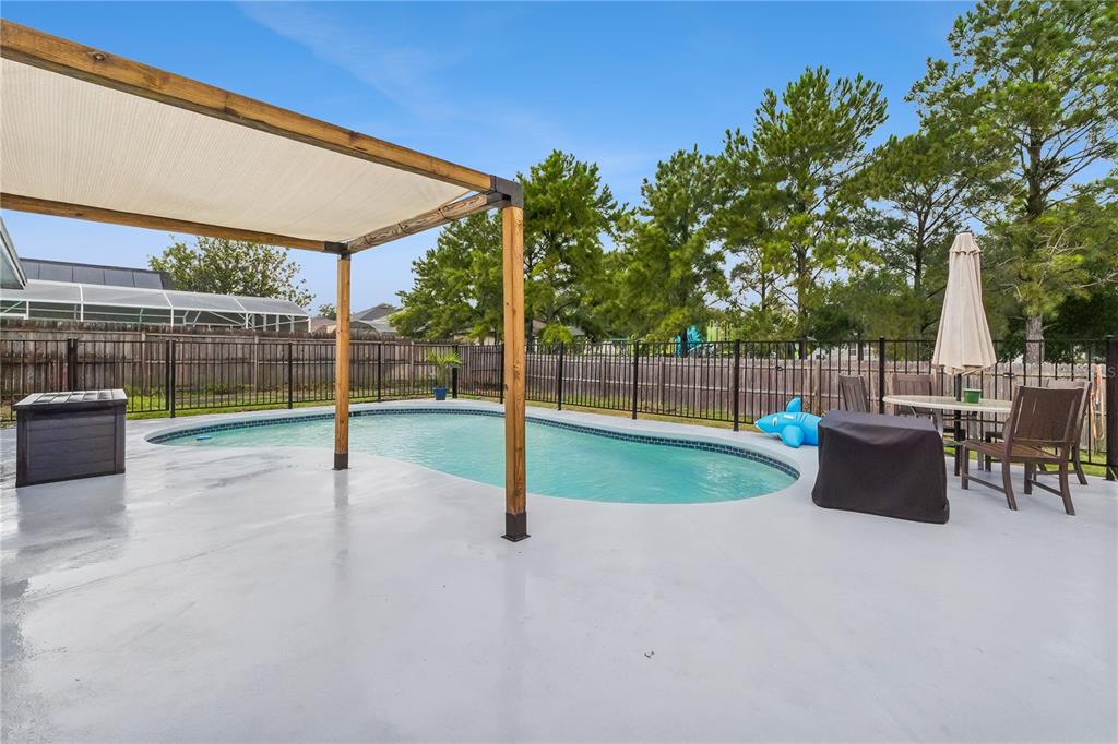 A backyard swimming pool features a wooden pergola, patio furniture, and a black metal fence — 5730 LOMA VISTA DRIVE W, DAVENPORT, FL