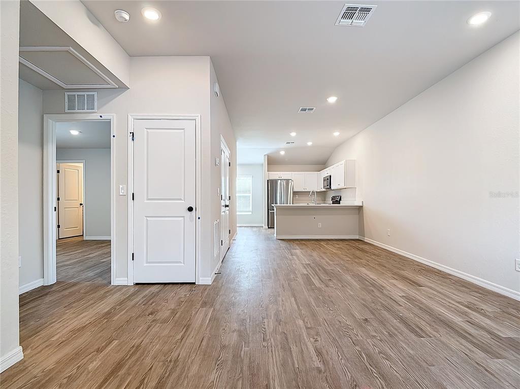 An open-concept living area features light wood-look flooring and a kitchen with white cabinetry — 1201 SE 24TH AVENUE, CAPE CORAL, FL