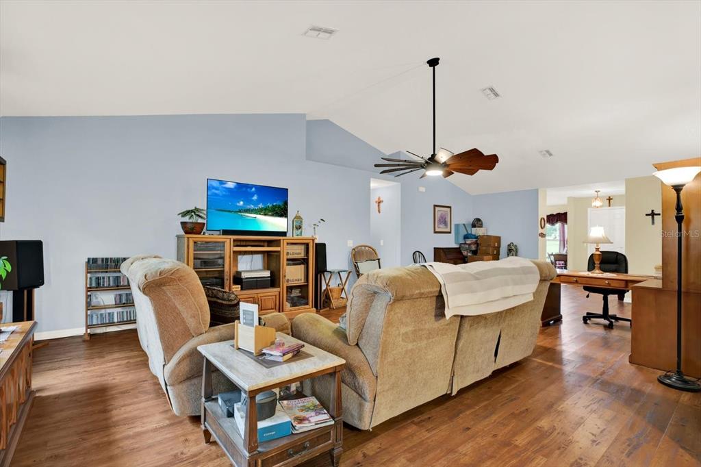 A living room features light blue walls, wood flooring, a ceiling fan, and beige furniture — 9086 MANCHESTER STREET, SPRING HILL, FL