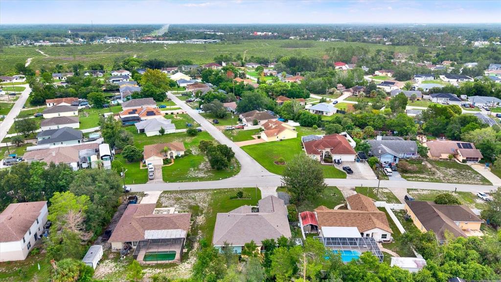 An aerial view shows a suburban neighborhood with single-family homes, paved streets, and green lawns — 9086 MANCHESTER STREET, SPRING HILL, FL
