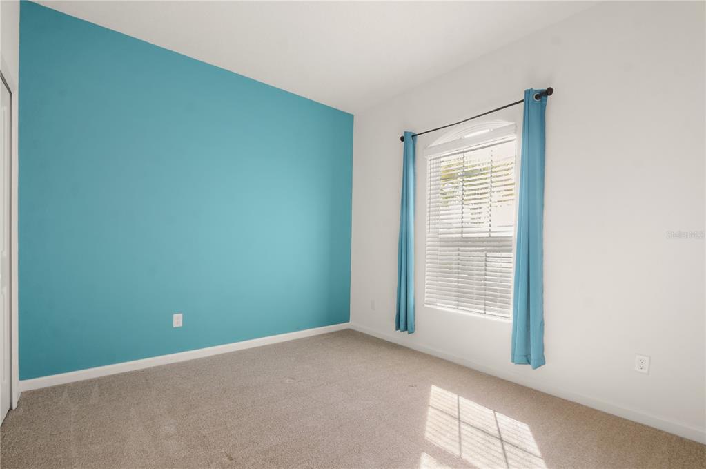 An empty bedroom features a blue accent wall, beige carpeting, and a window with curtains — 1078 CHELAN FALLS DRIVE, DELAND, FL