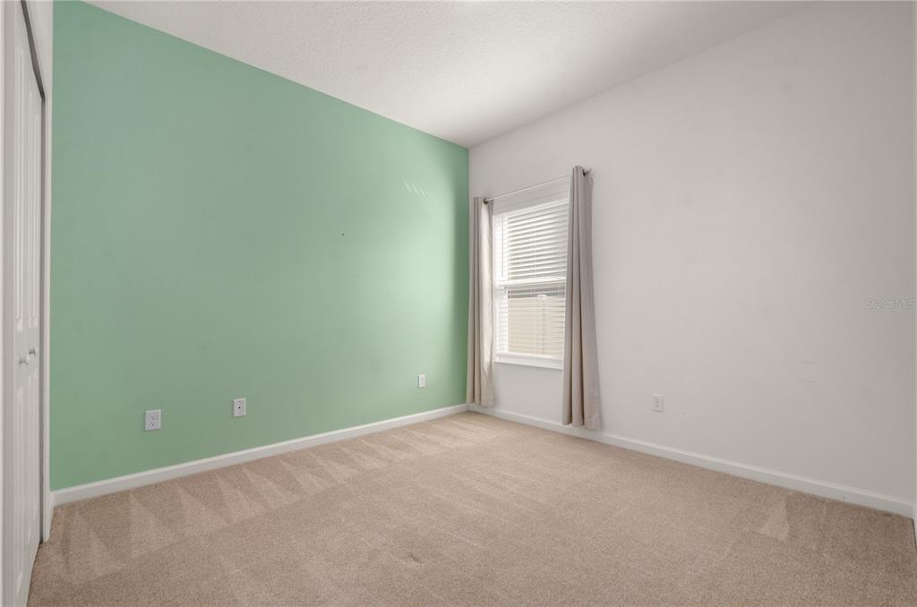 An empty bedroom features beige carpeting, white walls, and one mint green accent wall — 1078 CHELAN FALLS DRIVE, DELAND, FL
