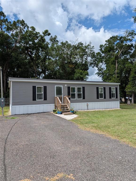 A gray manufactured home with white skirting and a small wooden porch sits on gravel — 4920 SE 146TH PLACE, SUMMERFIELD, FL