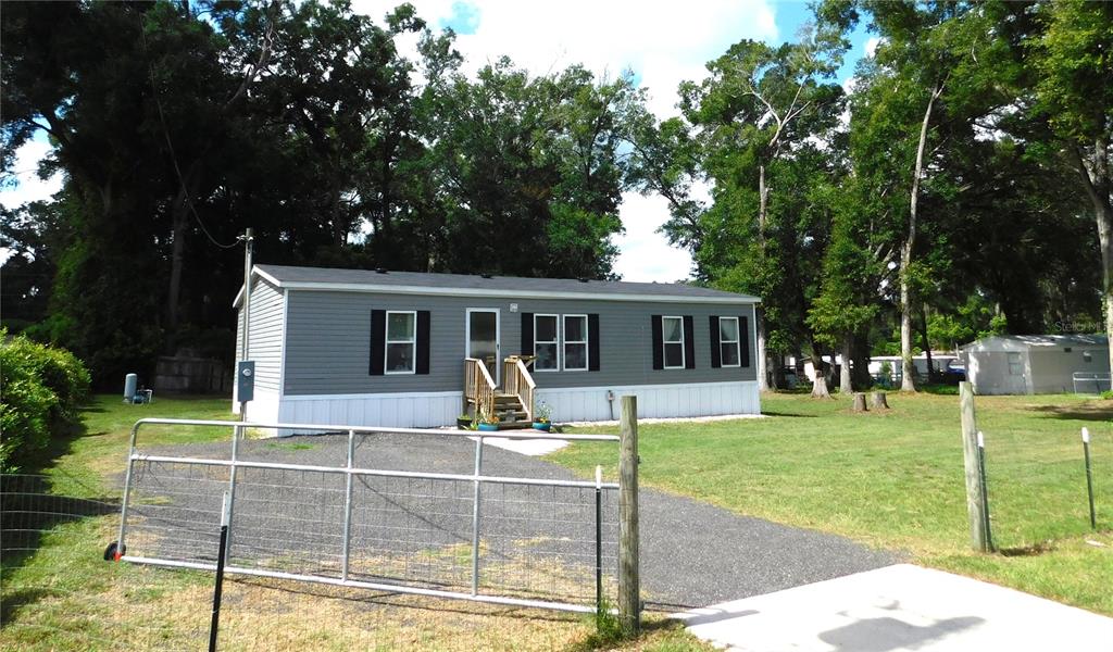 A gray manufactured home with white skirting sits on a grassy lot behind a gate — 4920 SE 146TH PLACE, SUMMERFIELD, FL