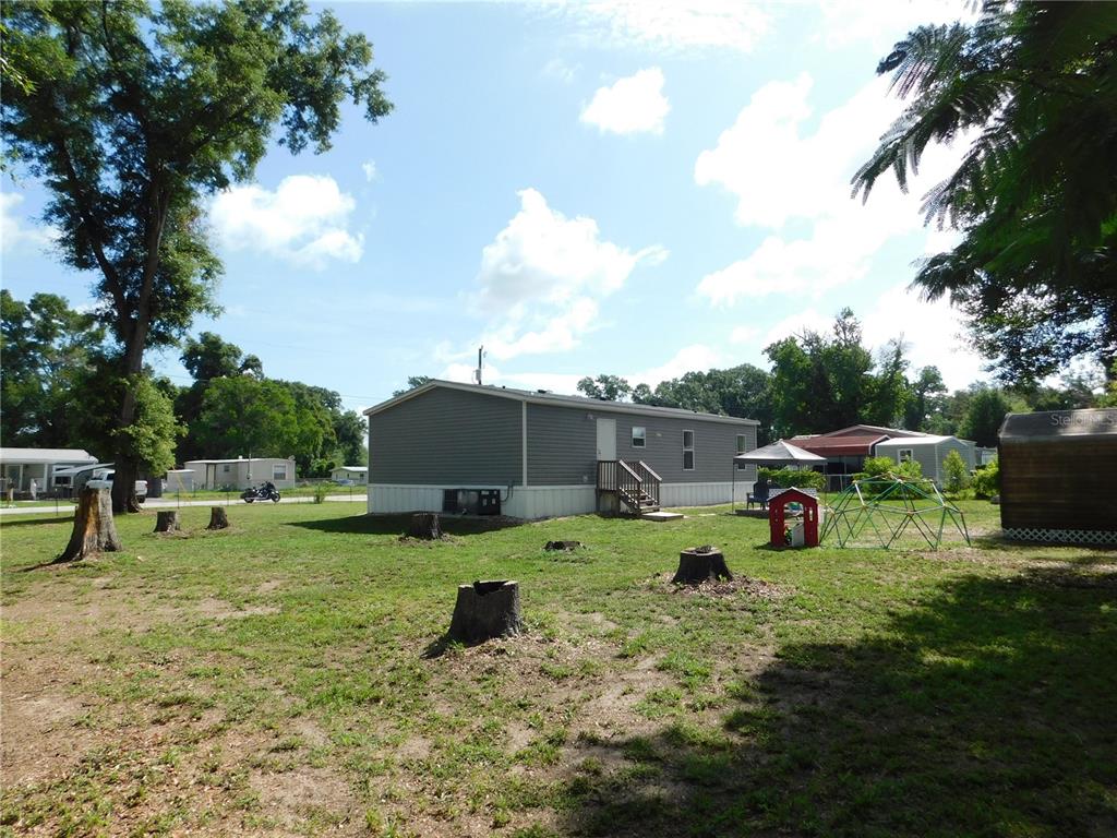 A gray manufactured home sits on a grassy lot with several tree stumps — 4920 SE 146TH PLACE, SUMMERFIELD, FL