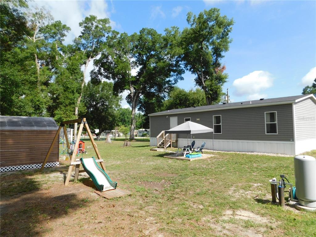 A backyard features a mobile home, a swing set with a slide, and a shed — 4920 SE 146TH PLACE, SUMMERFIELD, FL