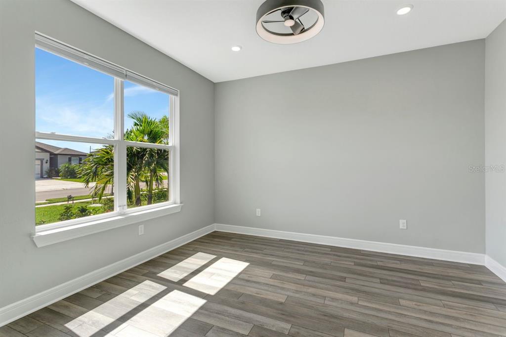 An empty room features gray walls, wood-look flooring, a ceiling fan, and a large window — 9909 LONGMEADOW AVENUE, PARRISH, FL