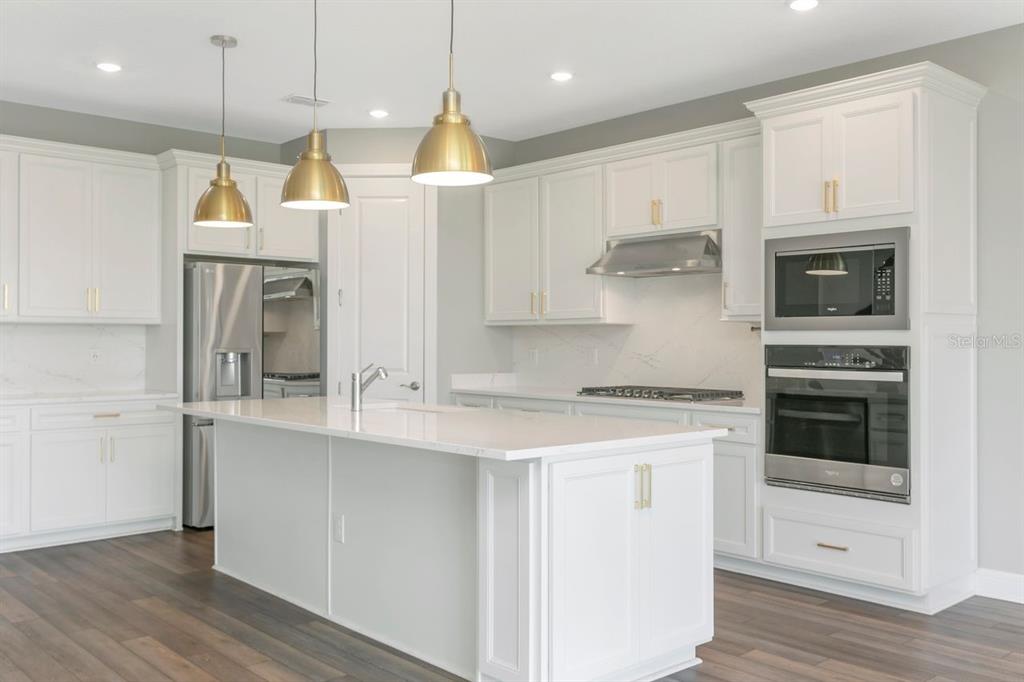 A modern kitchen features white cabinetry, a large center island, and stainless steel appliances — 9909 LONGMEADOW AVENUE, PARRISH, FL
