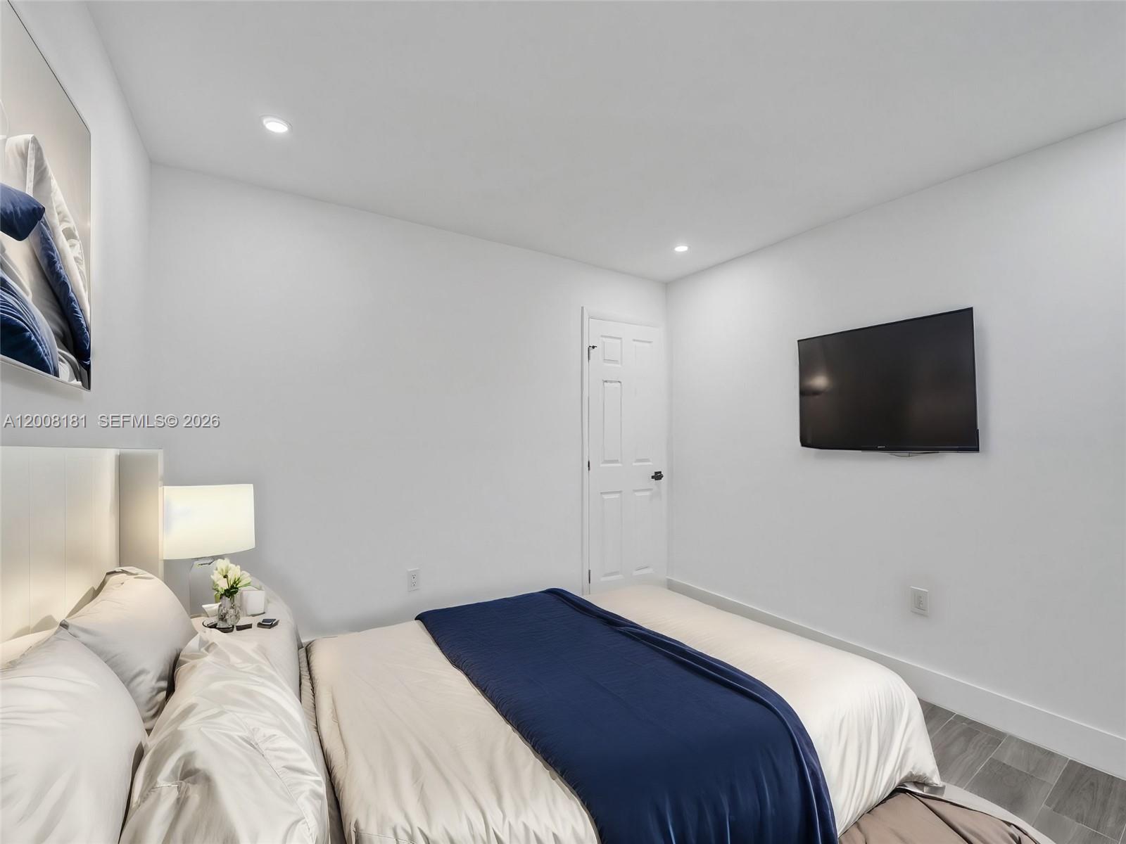 A bedroom features a bed with blue bedding, a wall-mounted television, and white walls — 5740 Mayo St # 0, Hollywood FL 33023, HOLLYWOOD, FL