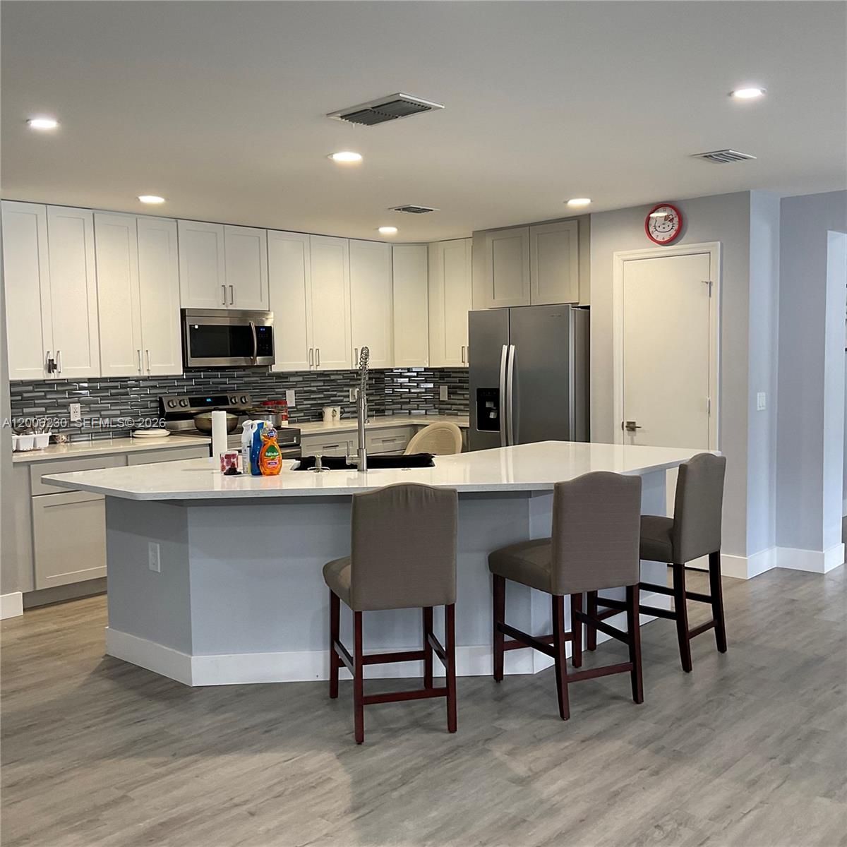 A modern kitchen features white cabinetry, a large island with bar stools, and grey flooring — 1903 Binnacle, Kissimmee FL 34744, KISSIMMEE, FL