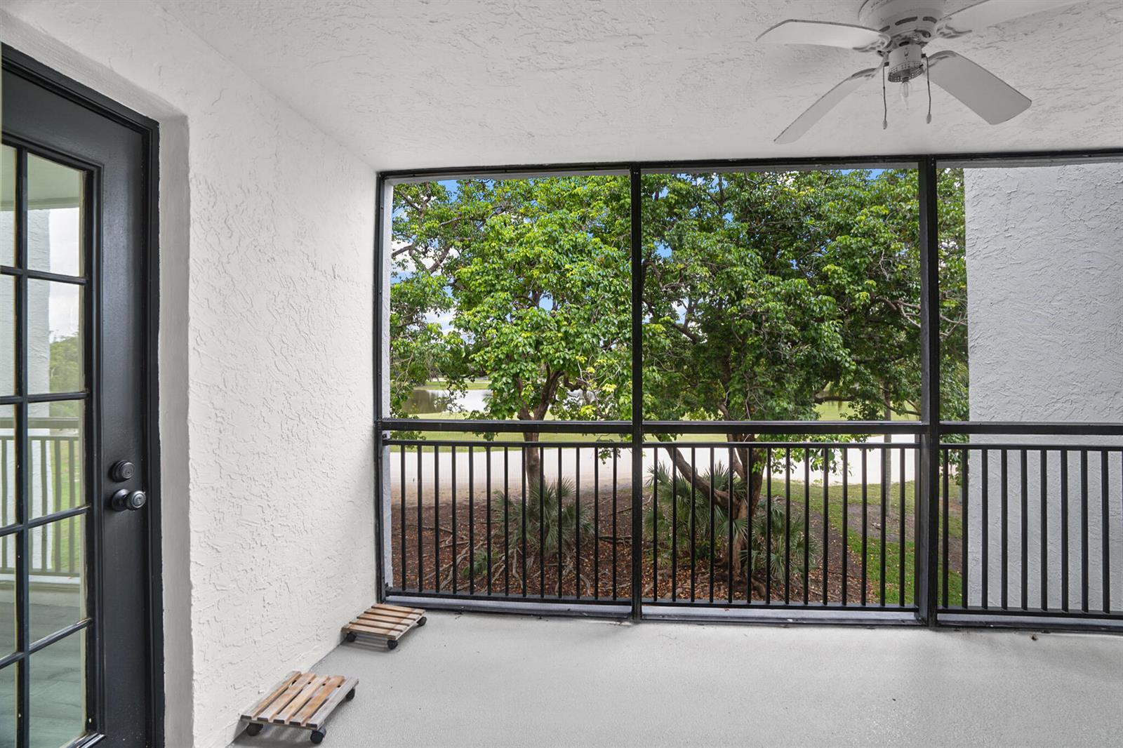 A screened-in balcony features a white ceiling fan, textured walls, and views of trees — 16141 Blatt Boulevard # 307, Weston FL 33326, WESTON, FL