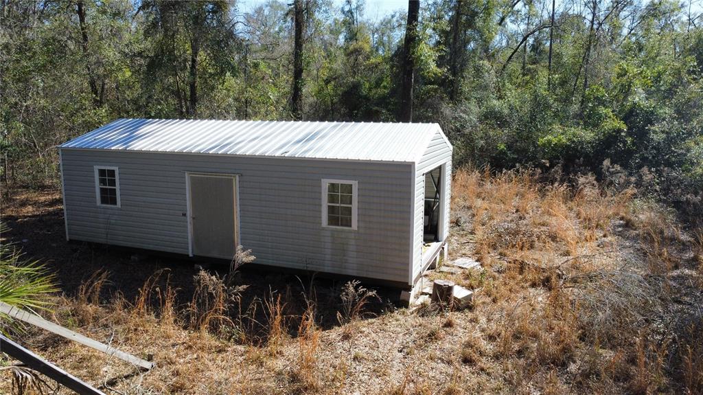 An exterior view of a rectangular shed with light gray siding and a metal roof — 268 SW LUKE PLACE, FORT WHITE, FL