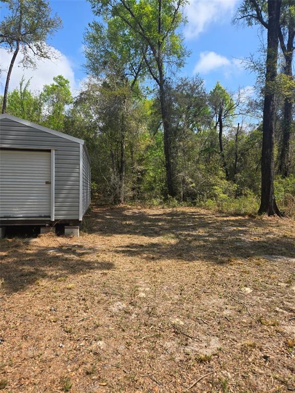 A gray metal storage shed sits on a cleared dirt lot surrounded by tall trees — 268 SW LUKE PLACE, FORT WHITE, FL