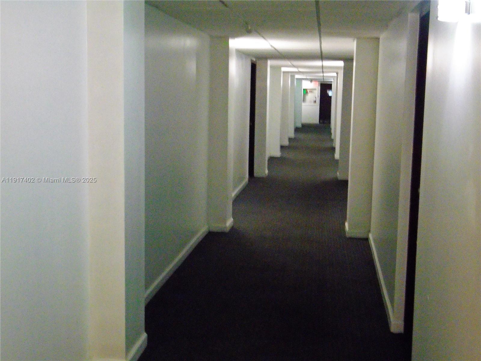 A long, narrow indoor hallway features white walls, dark carpeting, and recessed lighting — 4174 Inverrary Dr # 1004, Lauderhill FL 33319, LAUDERHILL, FL