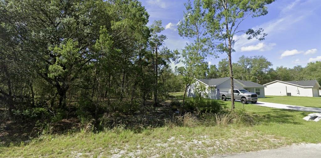 A vacant, wooded lot sits next to a single-story house with a driveway and truck — TBD FISHER WAY, OCKLAWAHA, FL