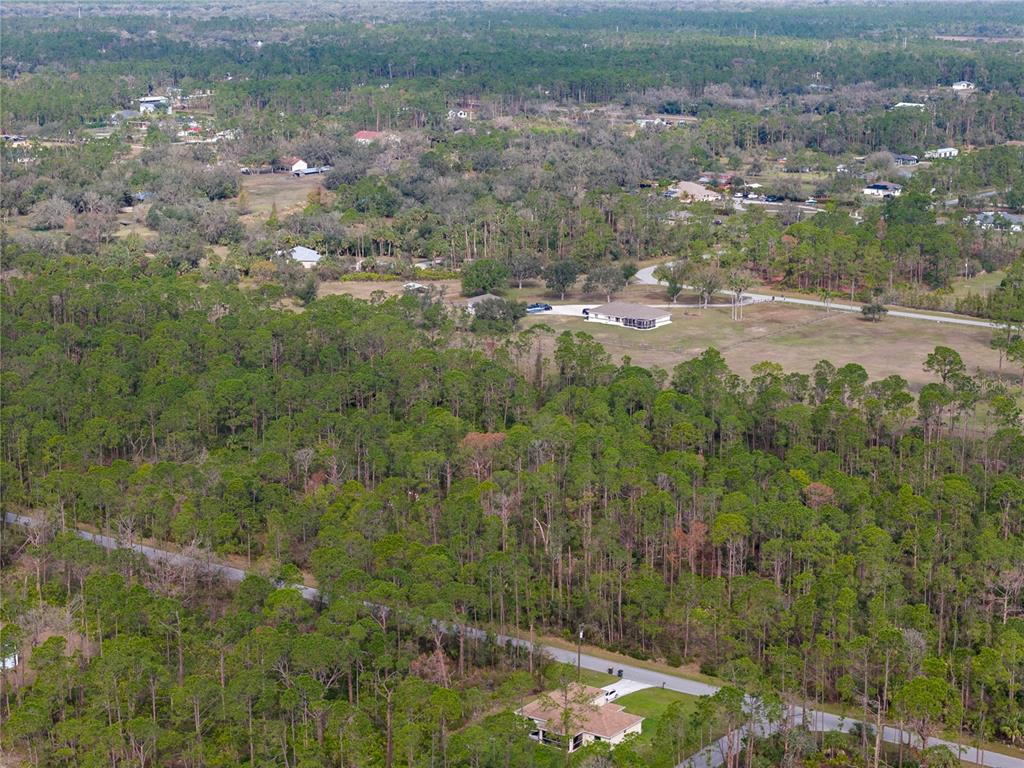 An aerial view shows a house surrounded by dense forest and a paved road — KAMSLER AVENUE, NORTH PORT, FL