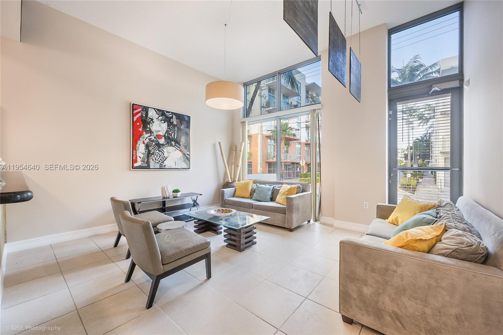 A modern living room features high ceilings, large windows, tile floors, and two gray sofas — 140 S Dixie Hwy, Hollywood FL 33020, HOLLYWOOD, FL
