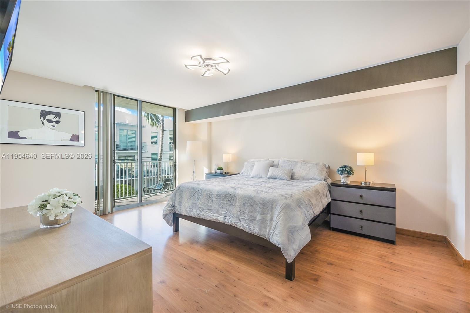 A bedroom features a bed, two nightstands, wood flooring, and a balcony with outdoor views — 140 S Dixie Hwy, Hollywood FL 33020, HOLLYWOOD, FL