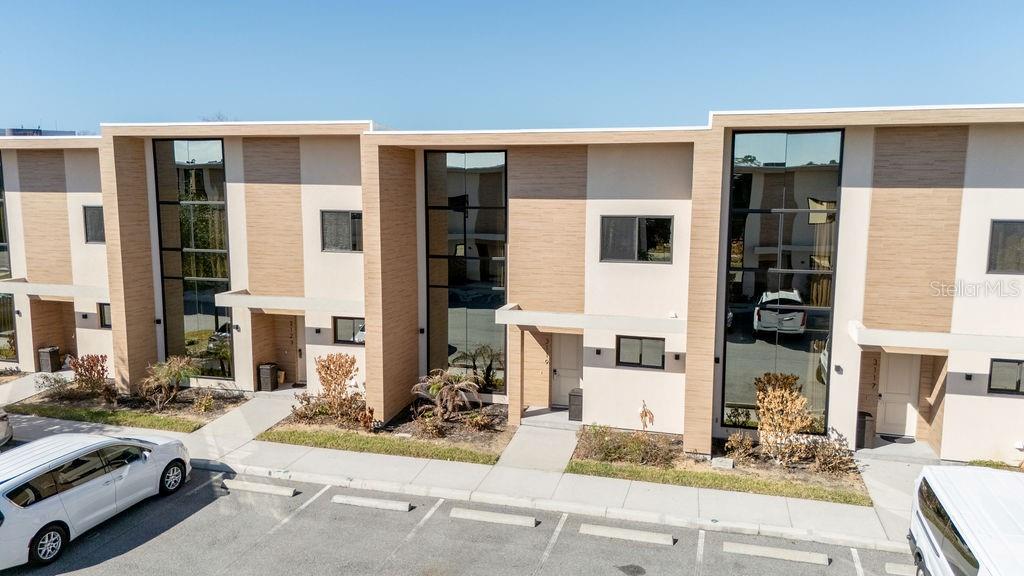 An exterior view of a modern multi-unit townhouse complex with light-colored siding and large windows — 3119 ROCKEFELLER WAY, KISSIMMEE, FL
