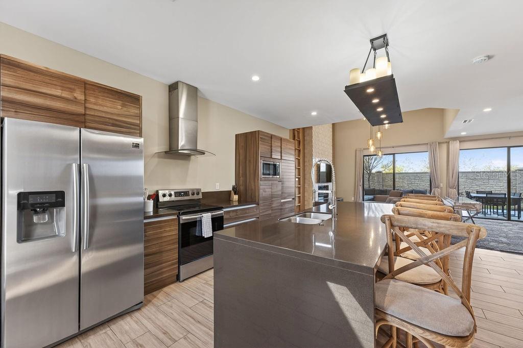 A modern kitchen features wood-grain cabinets, stainless steel appliances, and a large quartz island — 3119 ROCKEFELLER WAY, KISSIMMEE, FL