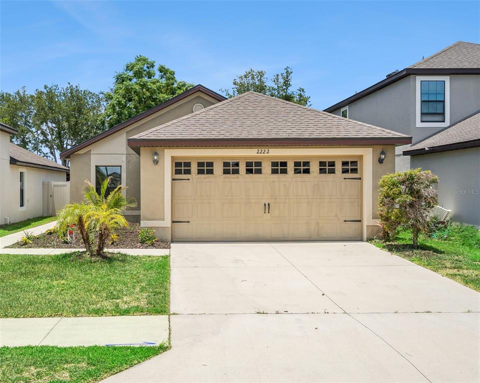 A single-story house features a tan stucco exterior, a two-car garage, and a concrete driveway — 2222 CASPIAN DRIVE, LAKELAND, FL