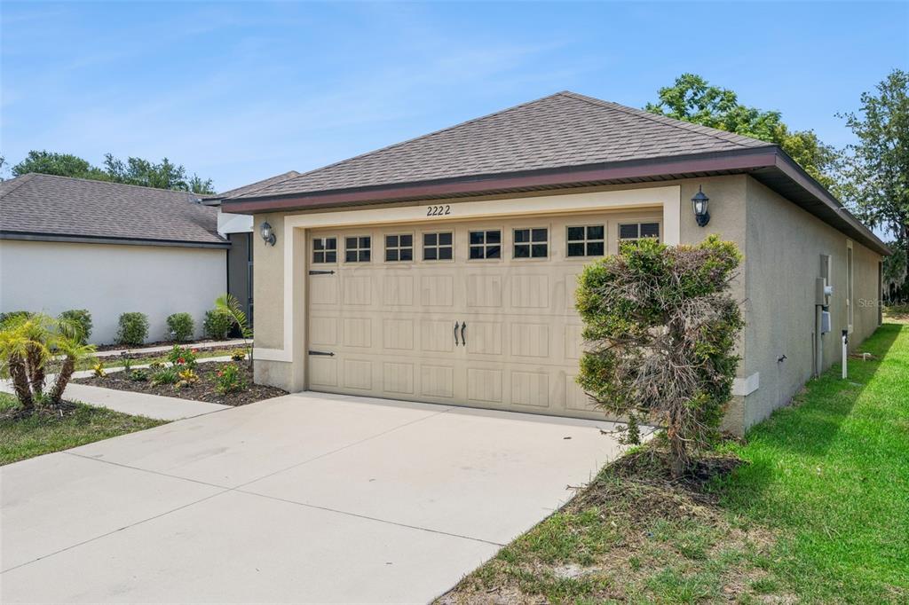 A beige house exterior features a two-car garage with windows and a concrete driveway — 2222 CASPIAN DRIVE, LAKELAND, FL