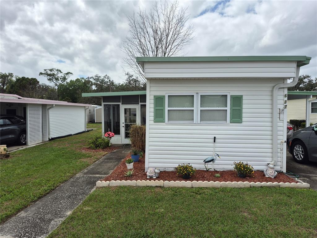 A white mobile home with green shutters and a small garden bed in the front — 637 MISTI DRIVE, LEESBURG, FL