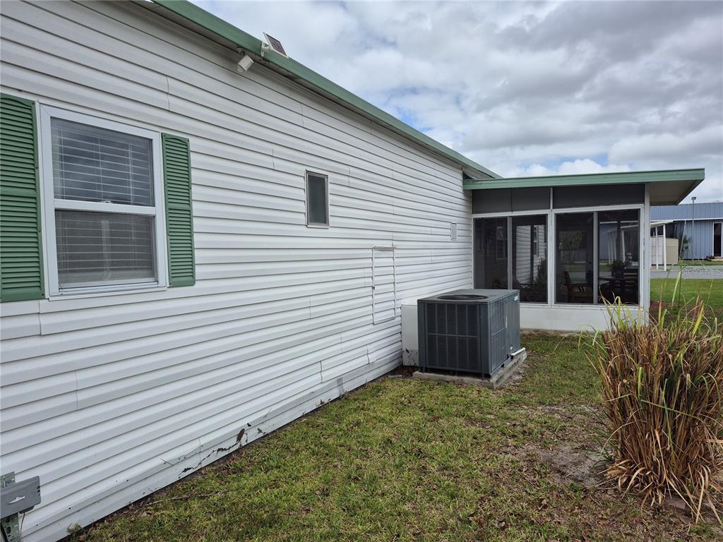 A side view of a white vinyl-sided house with a screened-in porch and AC unit — 637 MISTI DRIVE, LEESBURG, FL