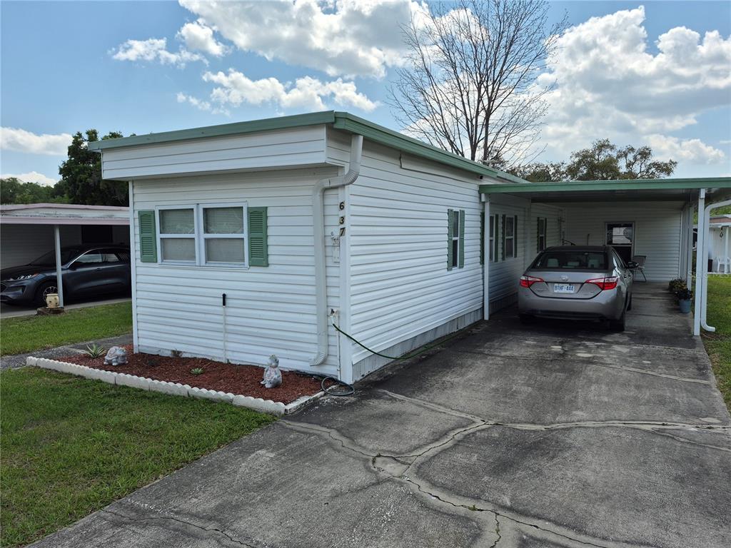 A white mobile home with green shutters and a carport sits on a concrete driveway — 637 MISTI DRIVE, LEESBURG, FL