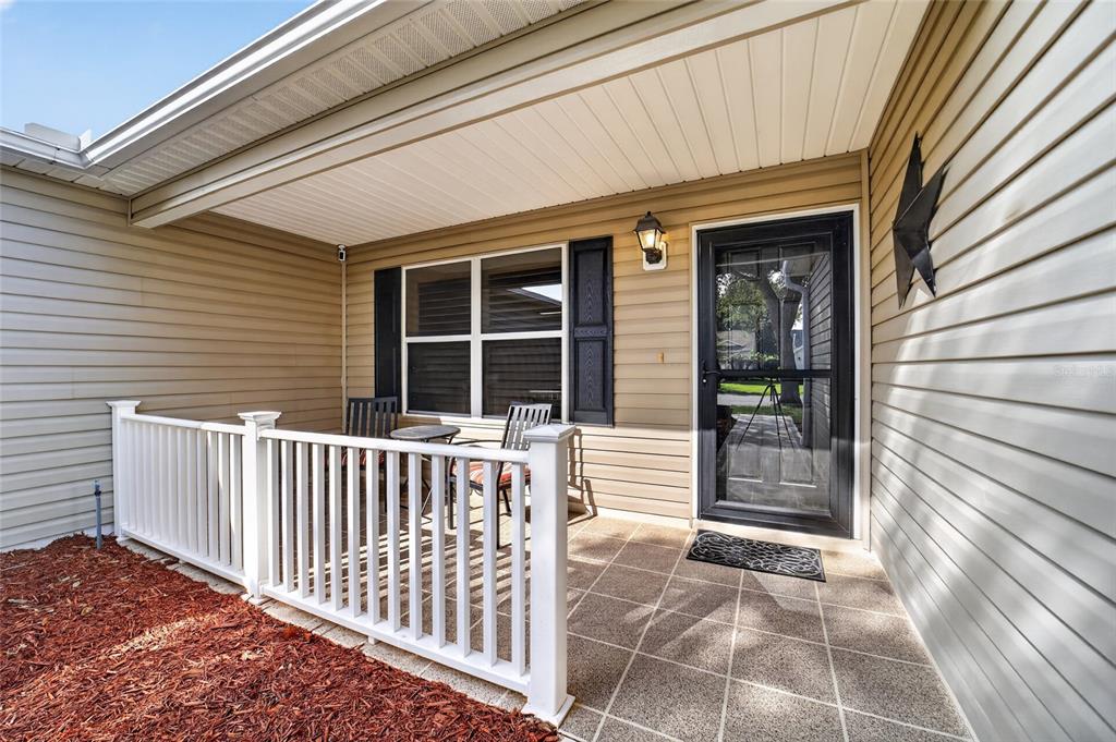 A covered front porch features tan siding, a white railing, and a tiled floor — 2240 LOWRY ROAD, THE VILLAGES, FL