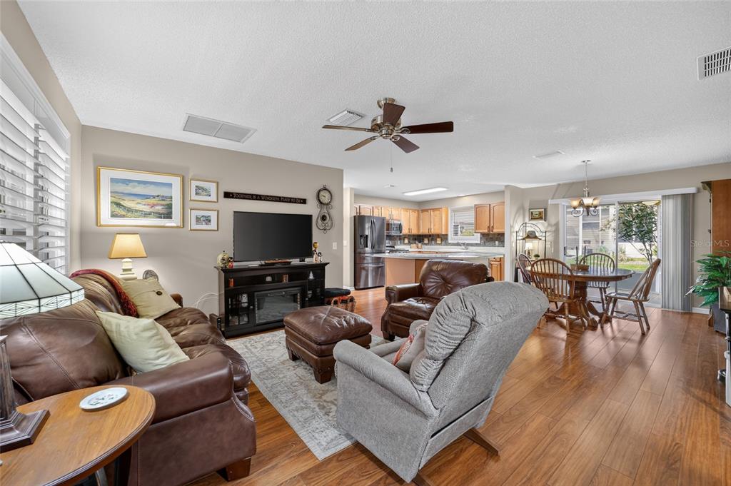 An open-concept living room and kitchen feature wood-look flooring, a ceiling fan, and leather furniture — 2240 LOWRY ROAD, THE VILLAGES, FL