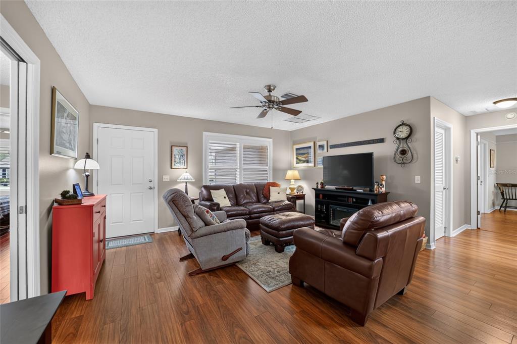 A living room features wood-look flooring, a ceiling fan, leather furniture, and a television console — 2240 LOWRY ROAD, THE VILLAGES, FL