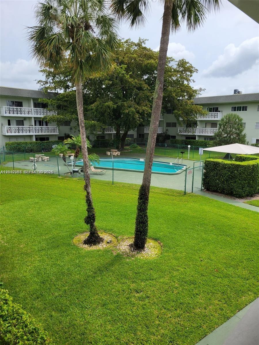 An outdoor view of a swimming pool surrounded by a fence, palm trees, and apartments — 4200 NW 3rd Ct # 224, Plantation FL 33317, PLANTATION, FL